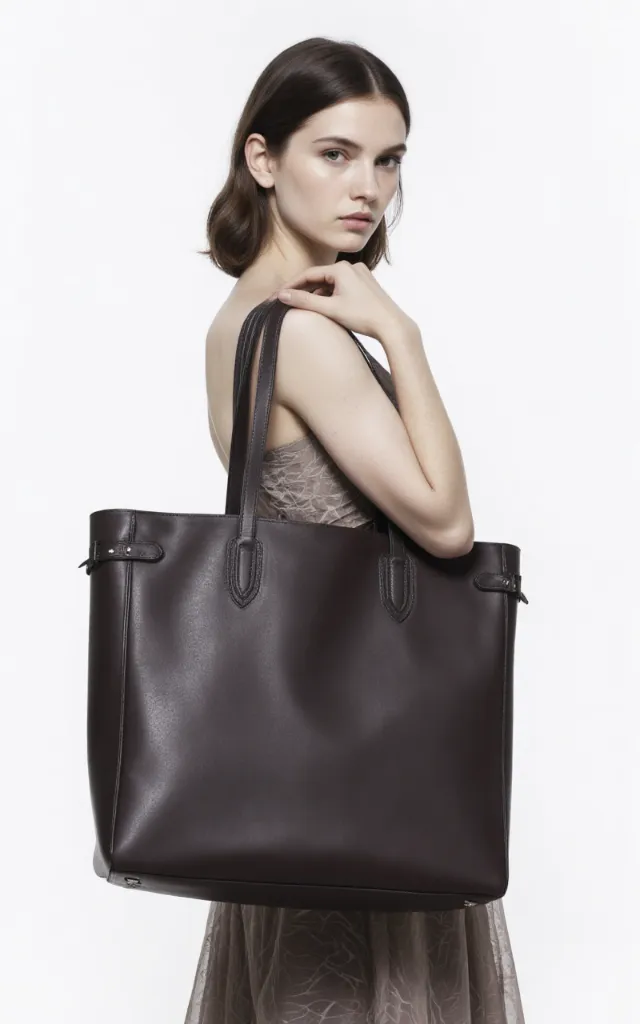 A French female model with a Large bag, wearing a dress, against a white background, in a front   facing close   up